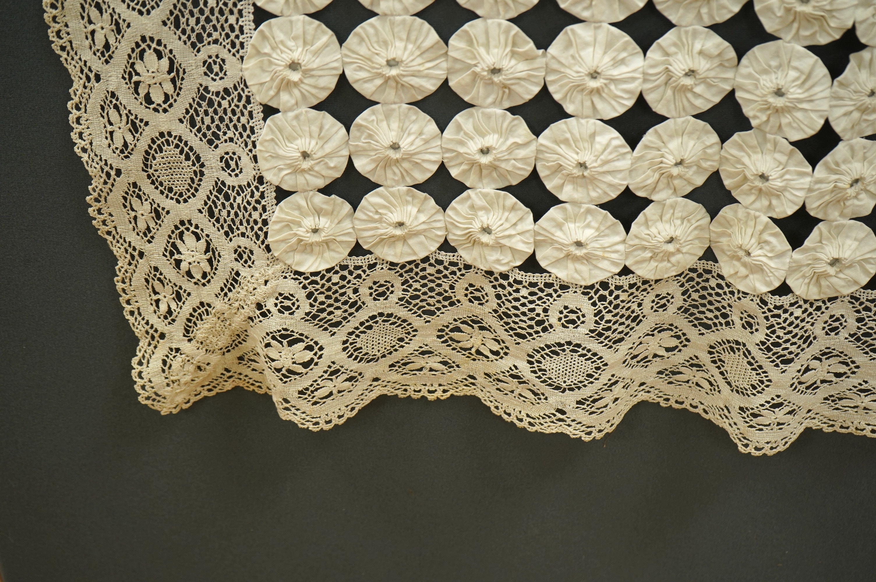 A late 19th early 20th century ‘YoYo’ puffy cream silk and cream bobbin lace quilt/bedcover, made with circles of silk, drawn together as a decorative gathered to top, then stitched together in panels and between wide bo